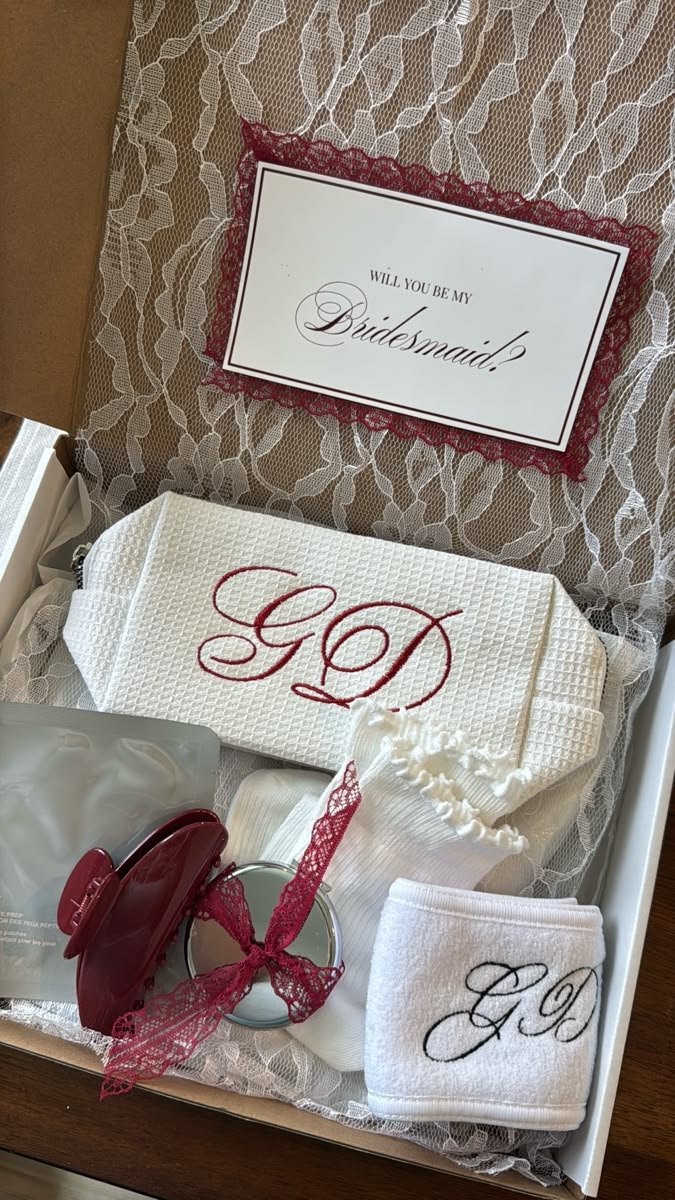 A bridesmaid proposal box with a Will You Be My Bridesmaid card, monogrammed pouch and headband, and burgundy lace details