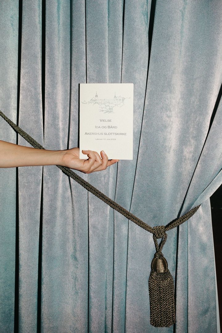 A wedding invitation held against a velvet curtain